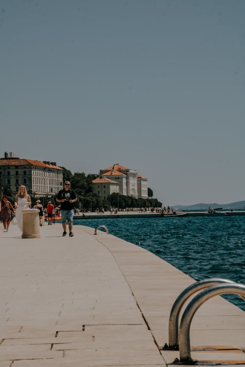 Free People stroll along Zadar's picturesque promenade by the Adriatic Sea on a sunny day, showcasing the coastal charm. Stock Photo
