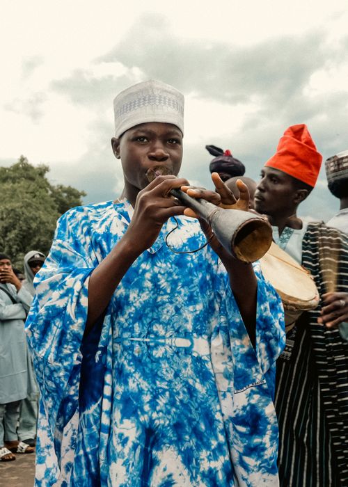 Free Young African musician in colorful attire playing a traditional wind instrument outdoors. Stock Photo