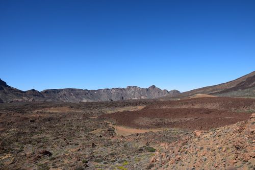 Free Rugged volcanic terrain with distant mountain range under a clear blue sky at daytime. Stock Photo