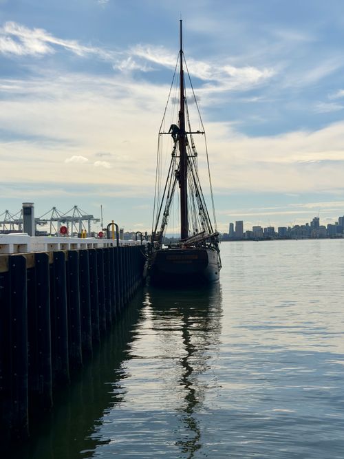 Free A classic sailing ship docked at Williamstown harbor with city skyline and cranes in the background. Stock Photo