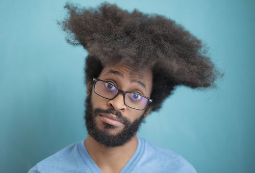Free Stylish man with afro hair and glasses posing against a blue background. Stock Photo