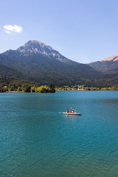 Free Two people kayaking in a pristine Greek lake with a mountain backdrop on a sunny day. Stock Photo
