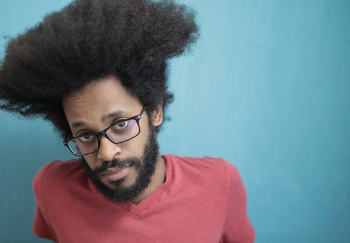 Free Casual portrait of a man with afro hair and glasses against a blue background. Stock Photo