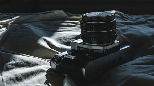 Free A vintage film camera resting on a bed with dramatic lighting creating shadows on a fabric surface. Stock Photo