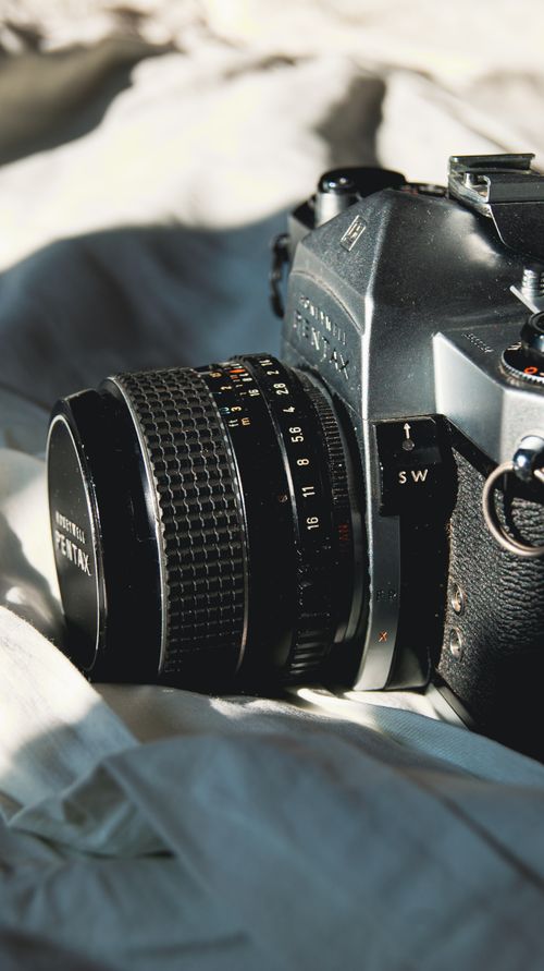 Free Close-up of a vintage Pentax camera resting on a soft white fabric, capturing light and shadows. Stock Photo