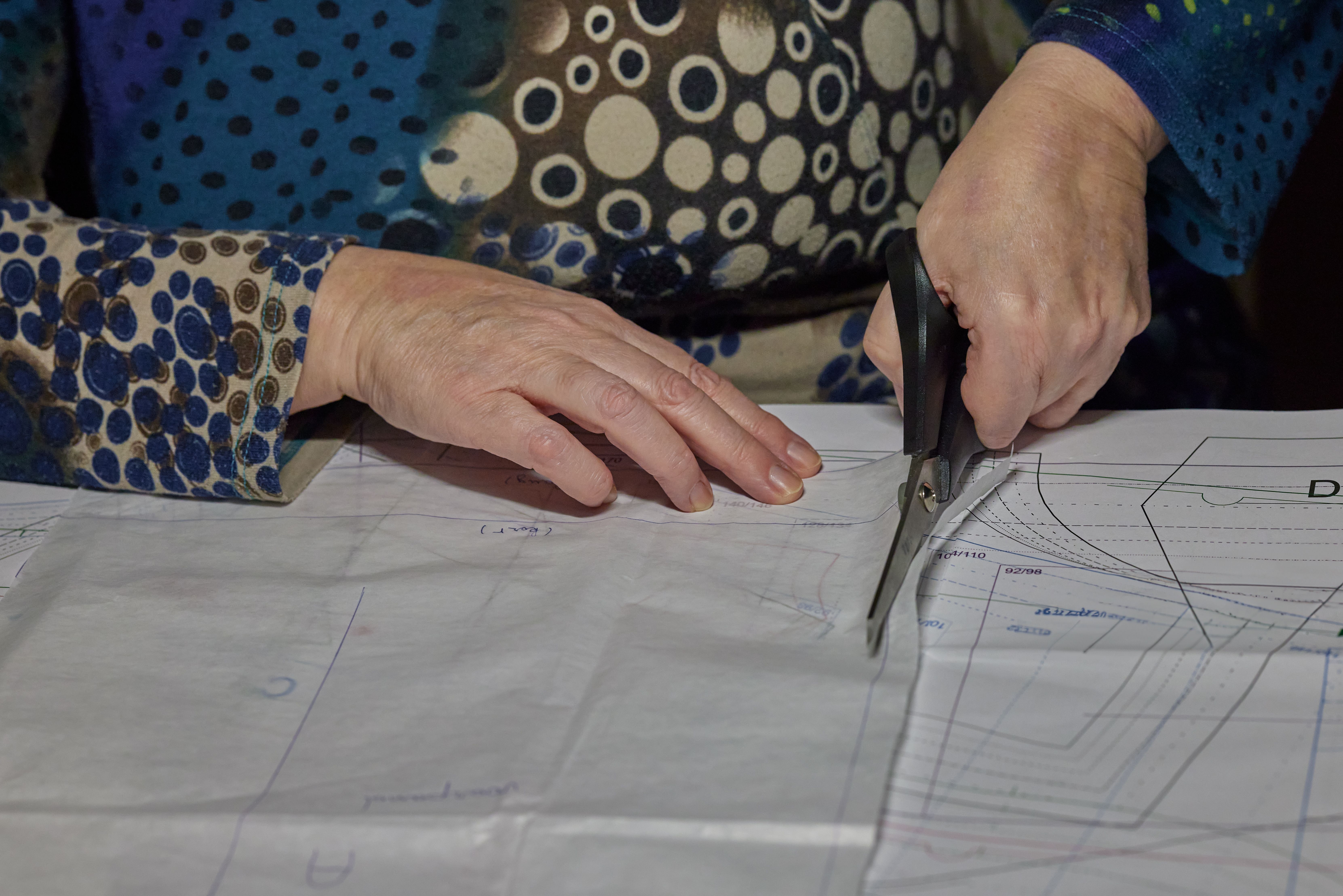 A detailed view of hands using scissors to cut a sewing pattern on fabric. DIY and crafting scene.