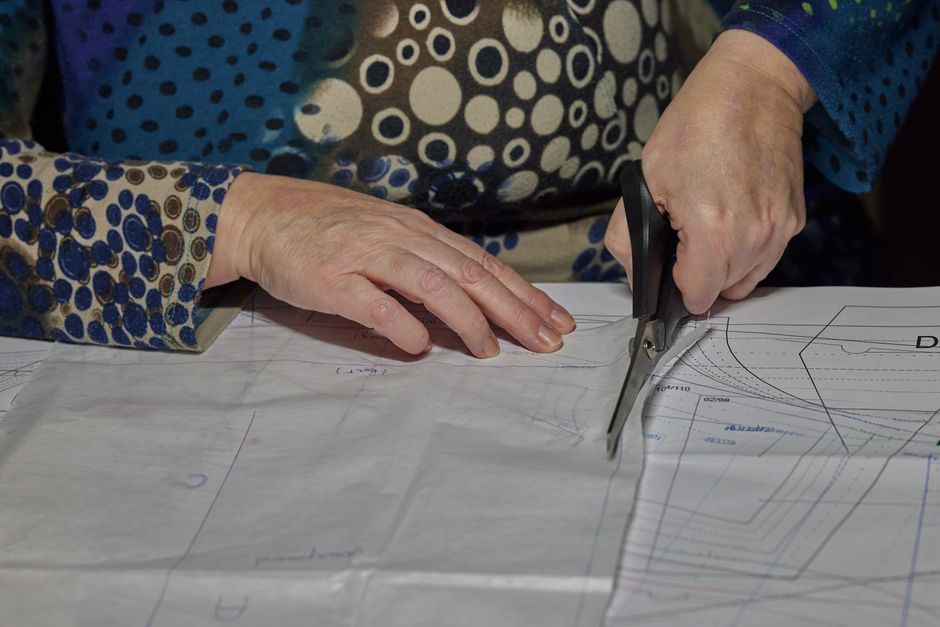A detailed view of hands using scissors to cut a sewing pattern on fabric. DIY and crafting scene.