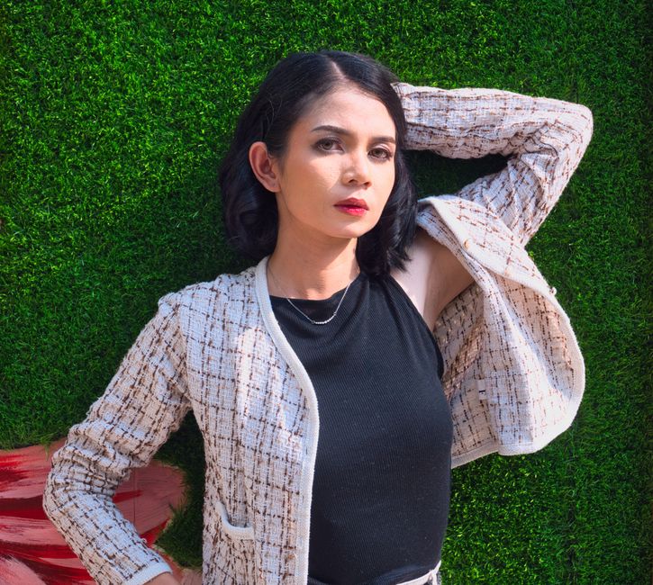 A woman in a cream tweed boucle jacket over a black top, styled in a modern editorial way against a green backdrop