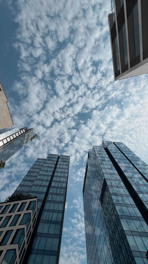 Free Upward view of modern glass skyscrapers with a cloudy blue sky backdrop. Stock Photo