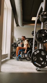 An adult male in a wheelchair working out in a modern gym, surrounded by weights.