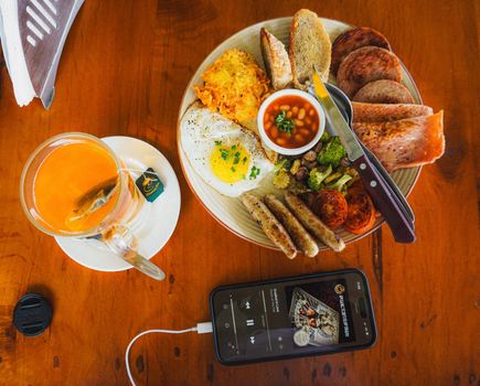 Delicious English breakfast with tea and smartphone on a wooden table.