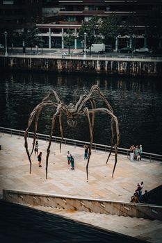 Visitors admire the iconic Maman sculpture beside the river in Bilbao, Spain.
