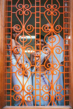 Three students in traditional attire stand behind ornate red bars in Varanasi, India.