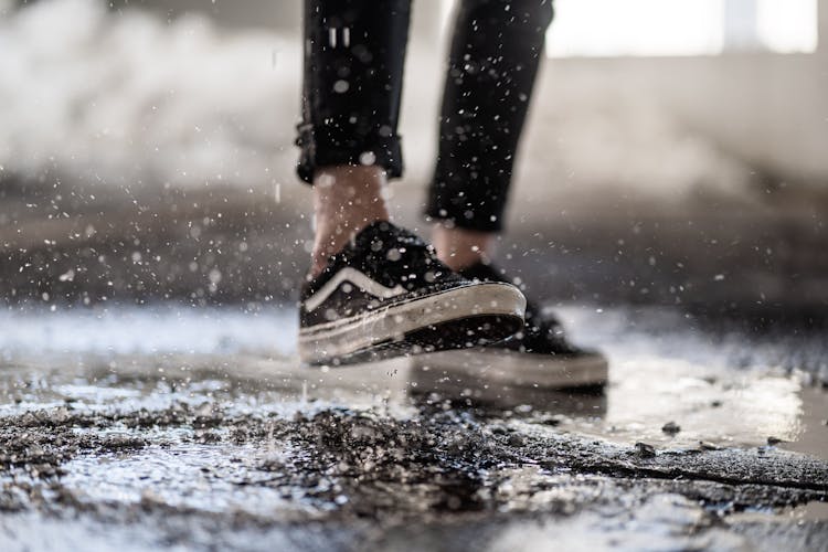 Crop Person Walking Through Puddles On Asphalt