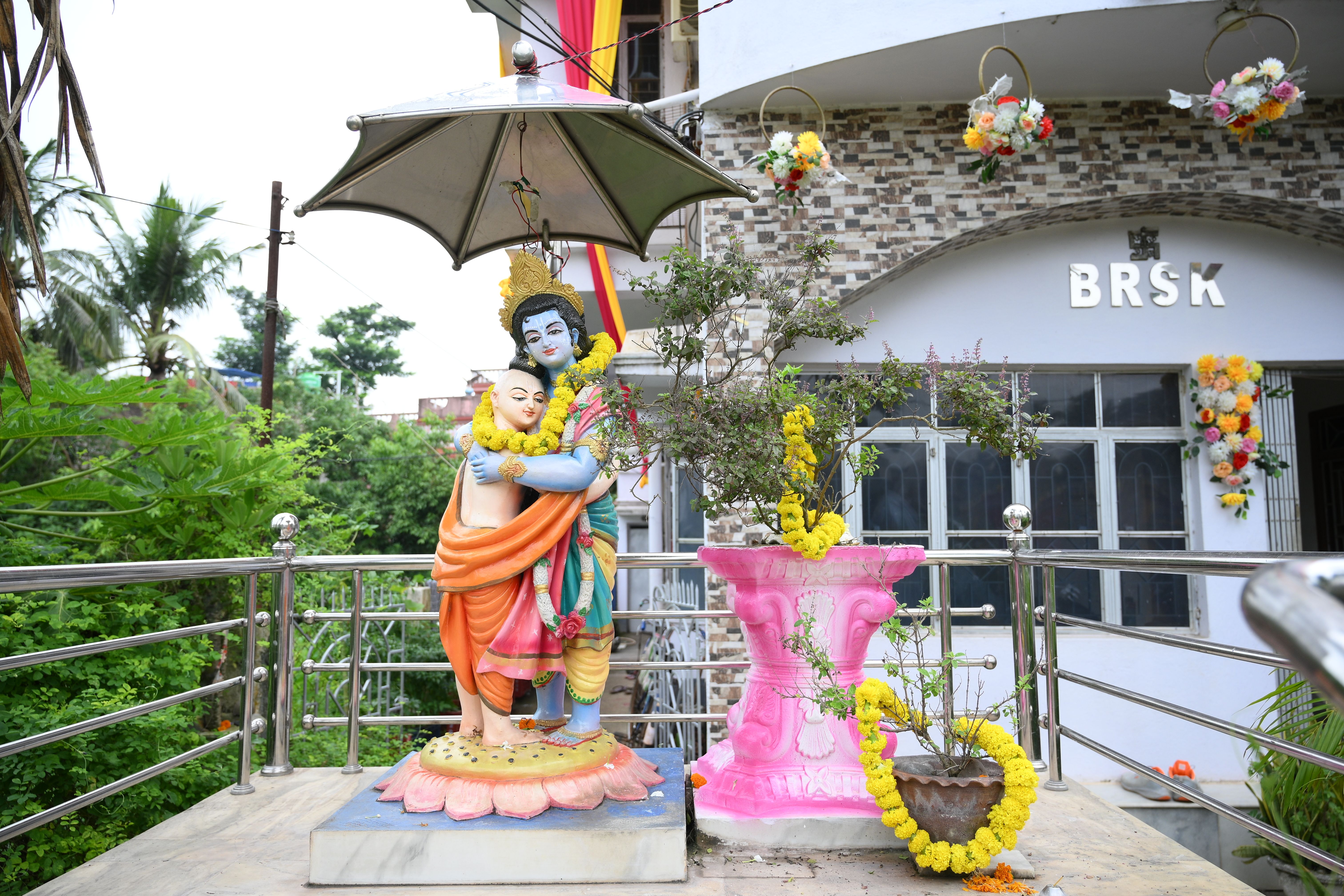 Colorful statues of Hindu deities Krishna and Sudama outdoors, under an umbrella with floral decor.