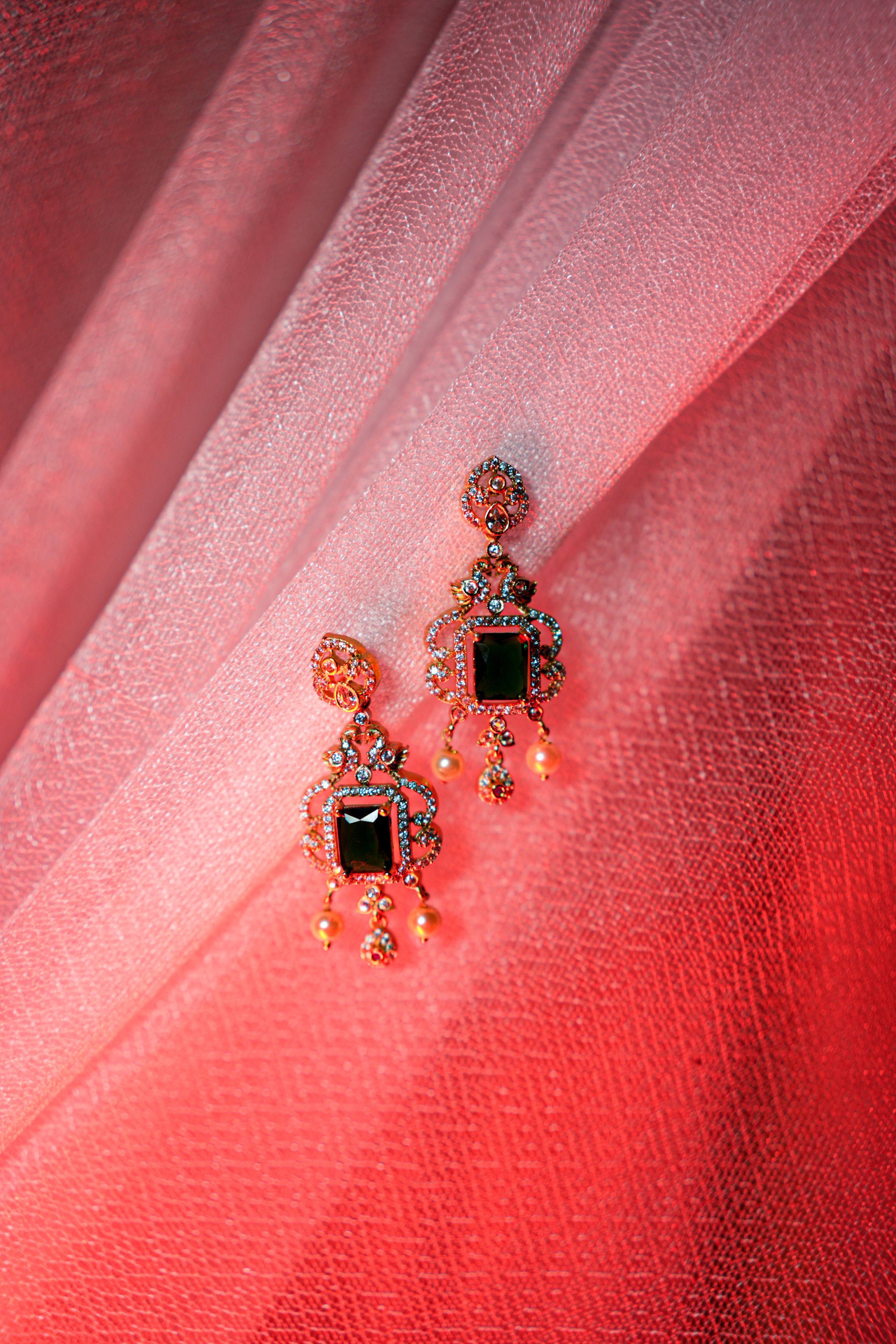 Rose-gold drop earrings with emerald-green and black stones on pink fabric