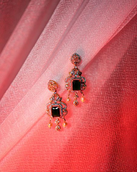 Rose-gold drop earrings with emerald-green and black stones on pink fabric