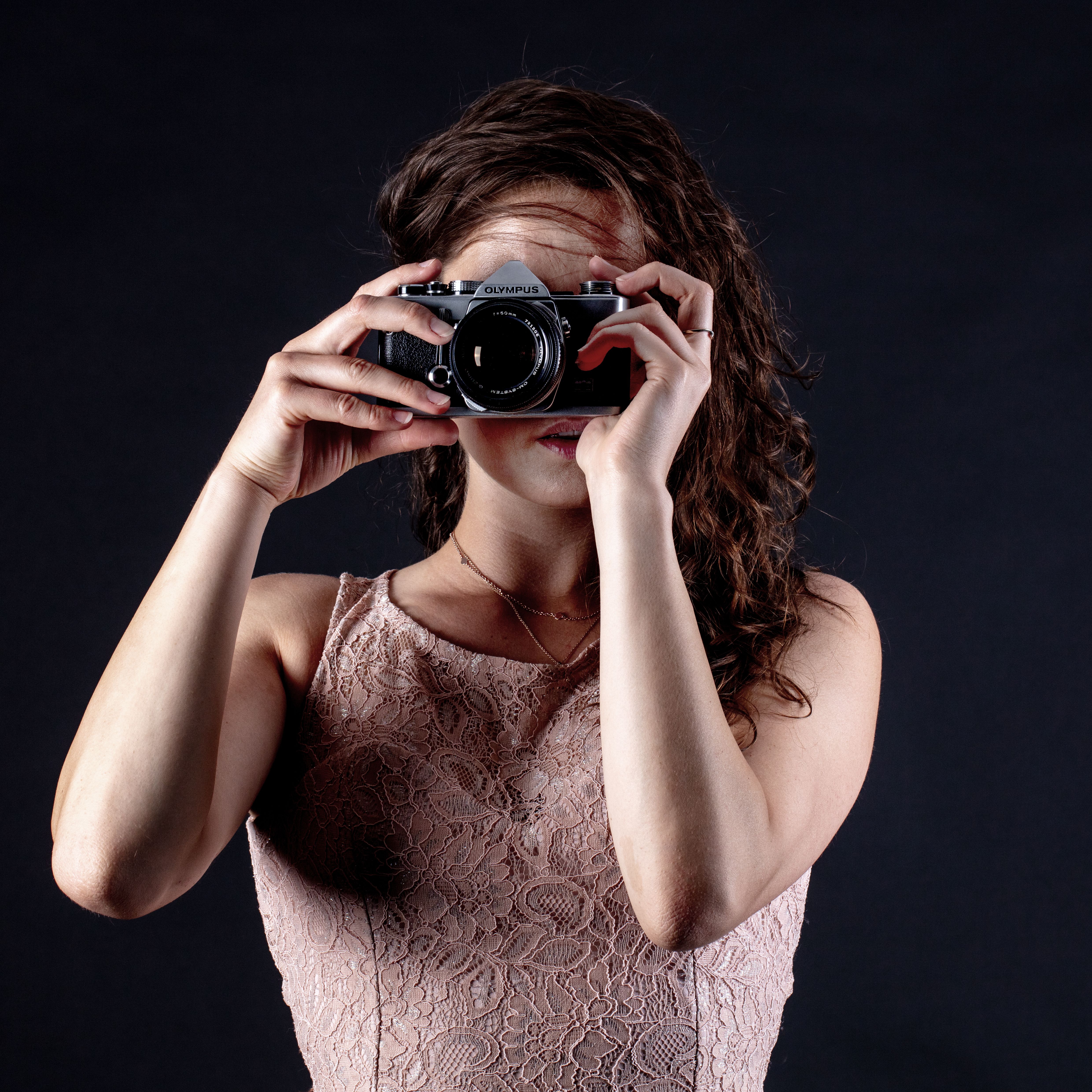 A woman in a lace dress holding a vintage camera against a dark background.