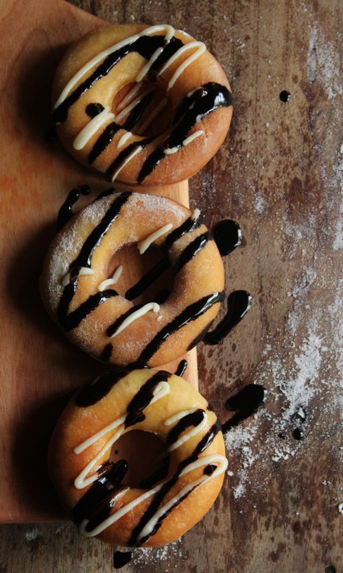 Free Three donuts with chocolate drizzle on a wooden board, perfect for dessert scenes. Stock Photo