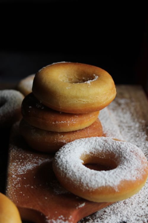 Free Close-up of fresh donuts dusted with powdered sugar, stacked on a wooden board. Stock Photo