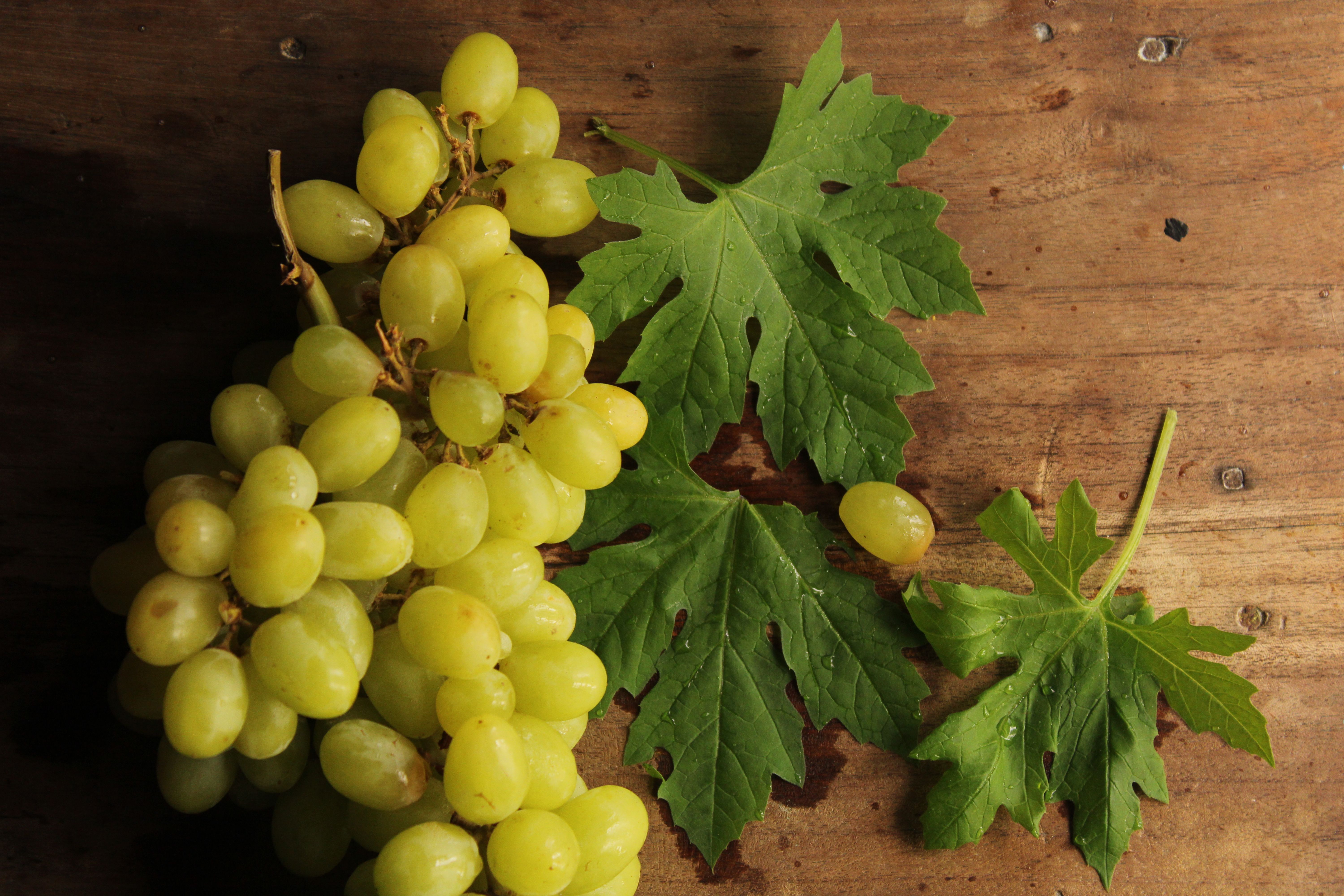 A cluster of green grapes with leaves on a rustic wooden background.