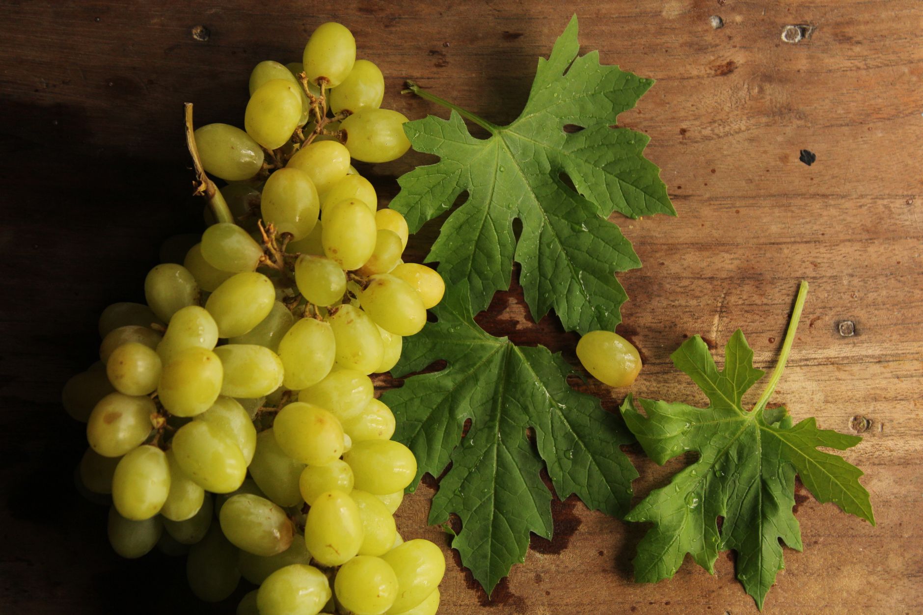 A cluster of green grapes with leaves on a rustic wooden background.