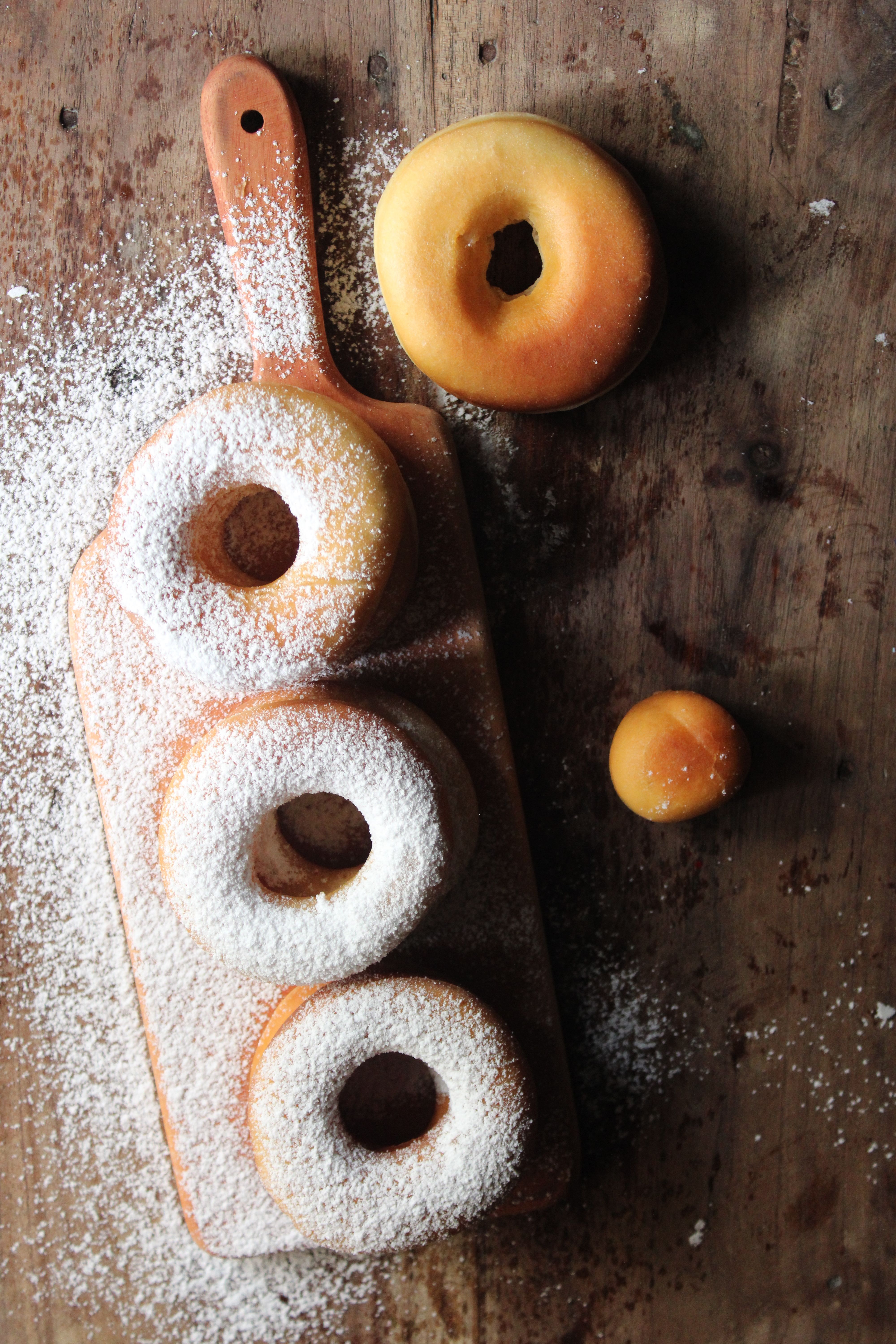 Flat lay of powdered sugar donuts on wooden board, perfect for breakfast themes.