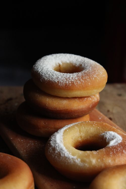 Free A stack of freshly baked donuts dusted with powdered sugar on a wooden board. Stock Photo