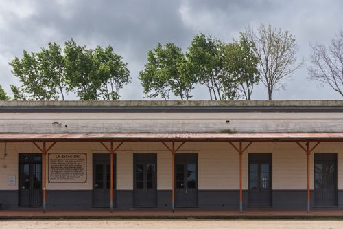 Free Facade of a vintage train station with trees and text sign under cloudy sky. Stock Photo