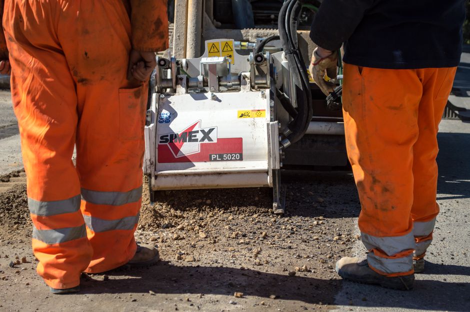 Two construction workers operating an asphalt paving machine during road maintenance.