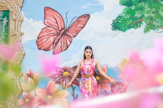 Woman in vibrant dress poses against a large floral and butterfly mural, capturing a blend of art and fashion.
