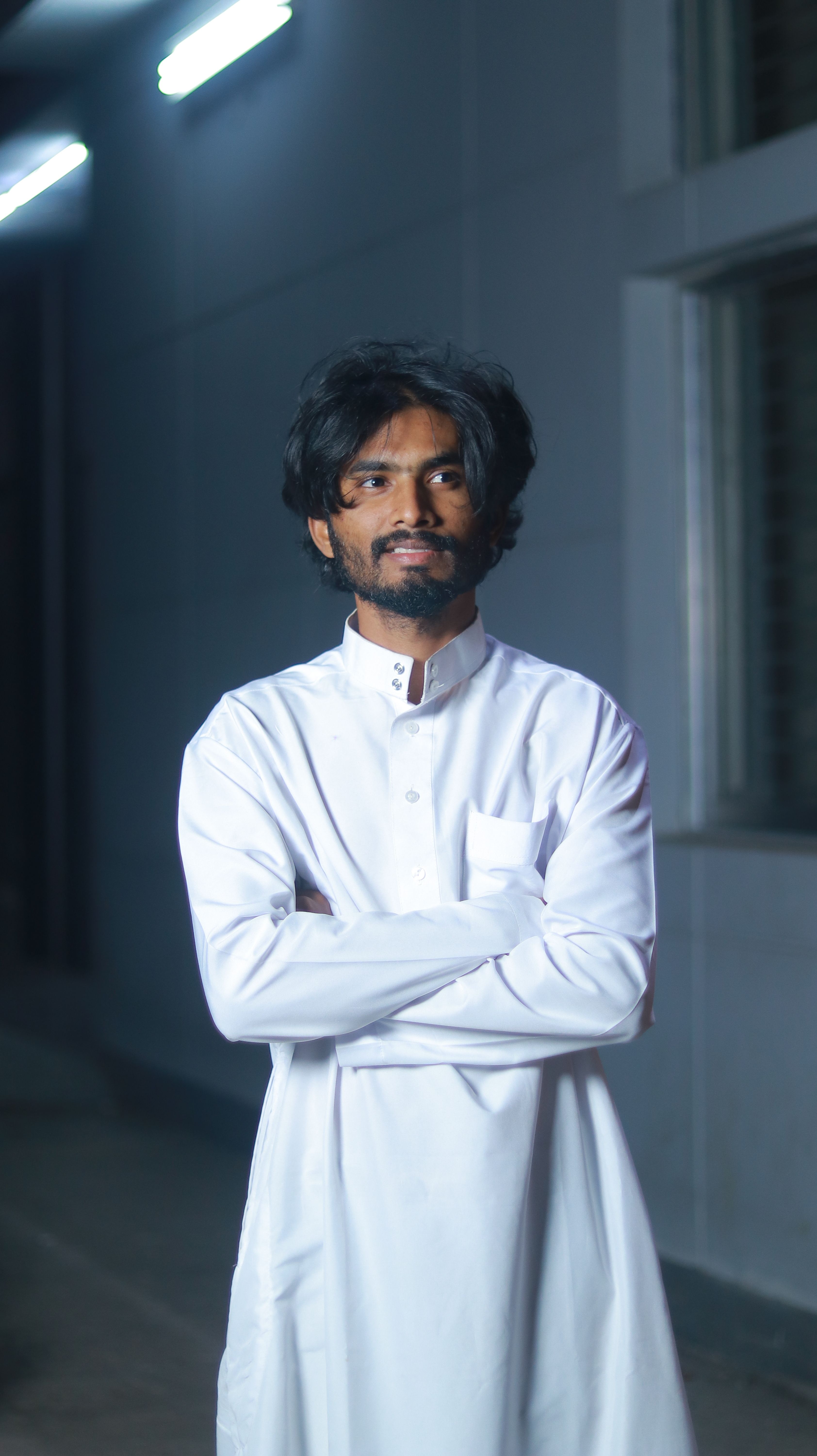 Man in traditional white clothing with arms crossed, standing outside at night.
