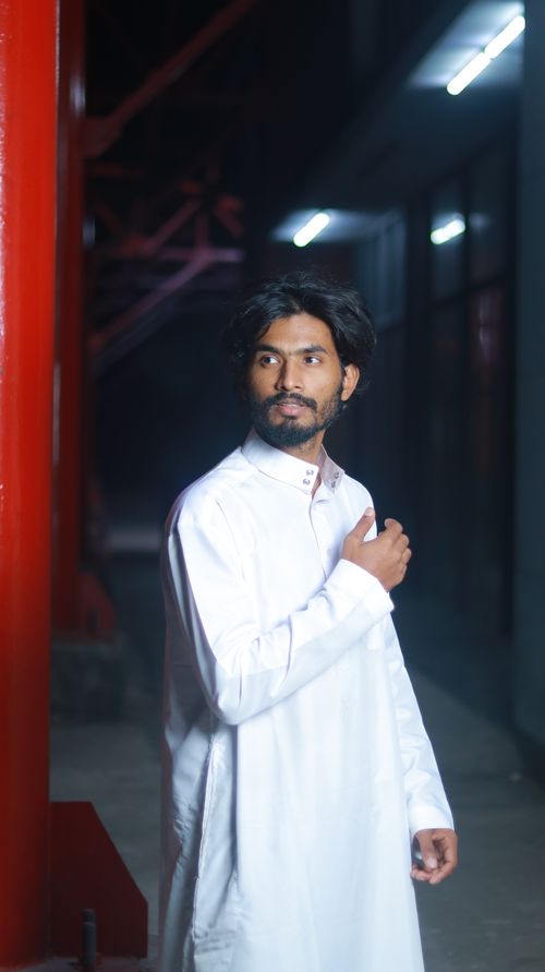 Free A man wearing traditional white clothing stands indoors, looking contemplatively to the side. Stock Photo