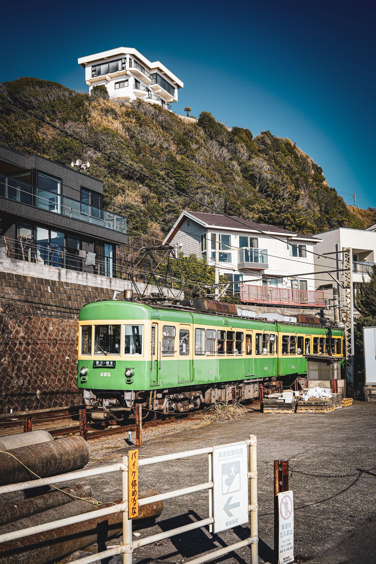 A green Enoden train passing hillside houses in Kamakura