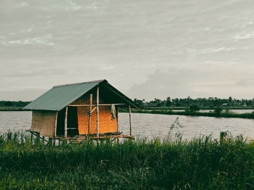 Free Tranquil scene of a small hut on a water body surrounded by lush greenery under a serene sky. Stock Photo