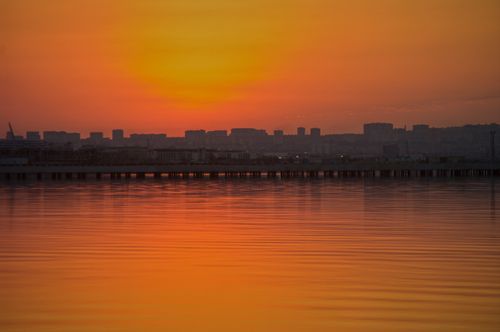 Free Stunning sunset view of Baku skyline with reflections in the Caspian Sea. Vibrant orange hues dominate the scene. Stock Photo