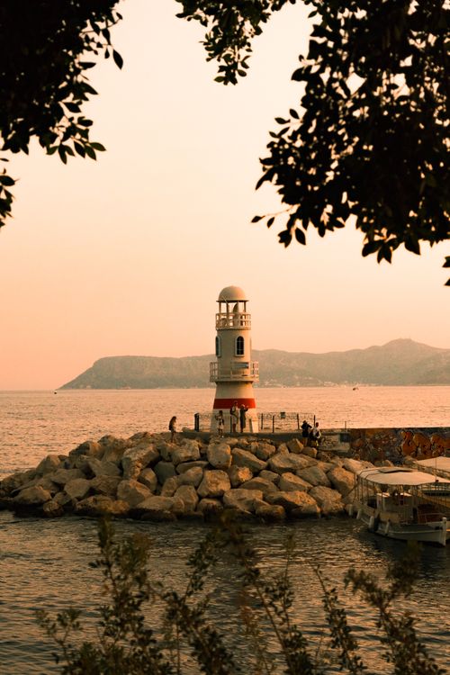Free A picturesque sunset over a lighthouse on a rocky shore, surrounded by gentle sea waves. Stock Photo