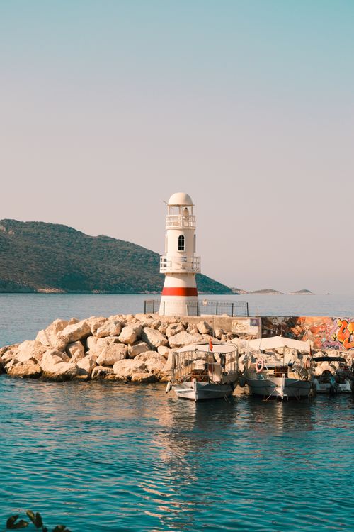 Free A picturesque lighthouse on rocky shore surrounded by blue waters and boats. Stock Photo