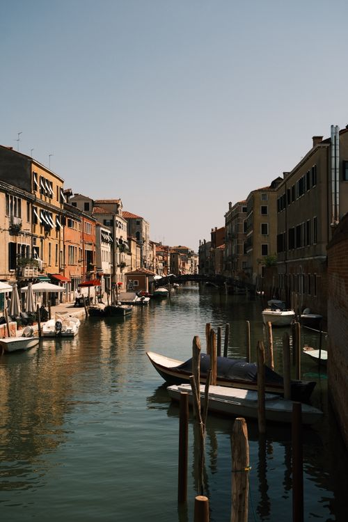 Free Beautiful view of a serene Venice canal with boats and vintage buildings under clear blue sky. Stock Photo