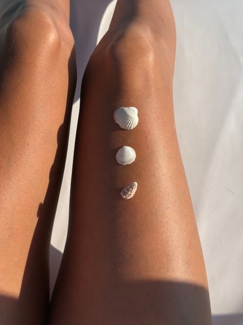 Free Three seashells arranged on sun-kissed legs at a beach. Perfect summer vibes. Stock Photo