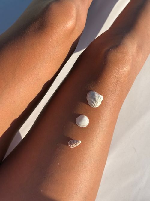 Free Sun-kissed legs decorated with seashells basking in the warm beach sunlight. Stock Photo