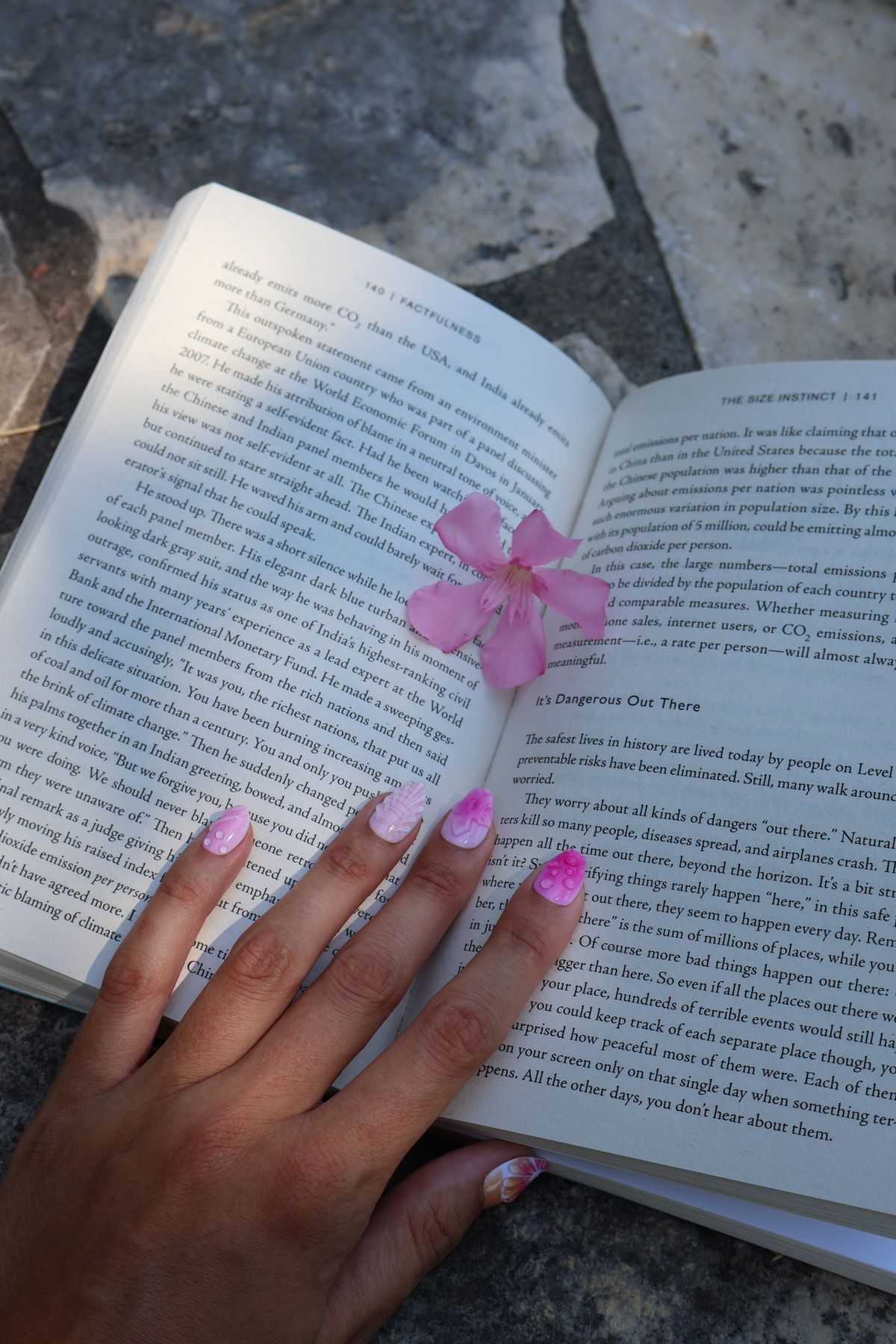 A close-up of a hand with pink nails gently holding an open book with a flower on it.