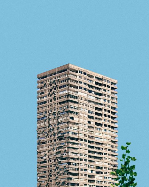 Free A minimalist photo of a high-rise building with a clear blue sky and tree leaves. Stock Photo