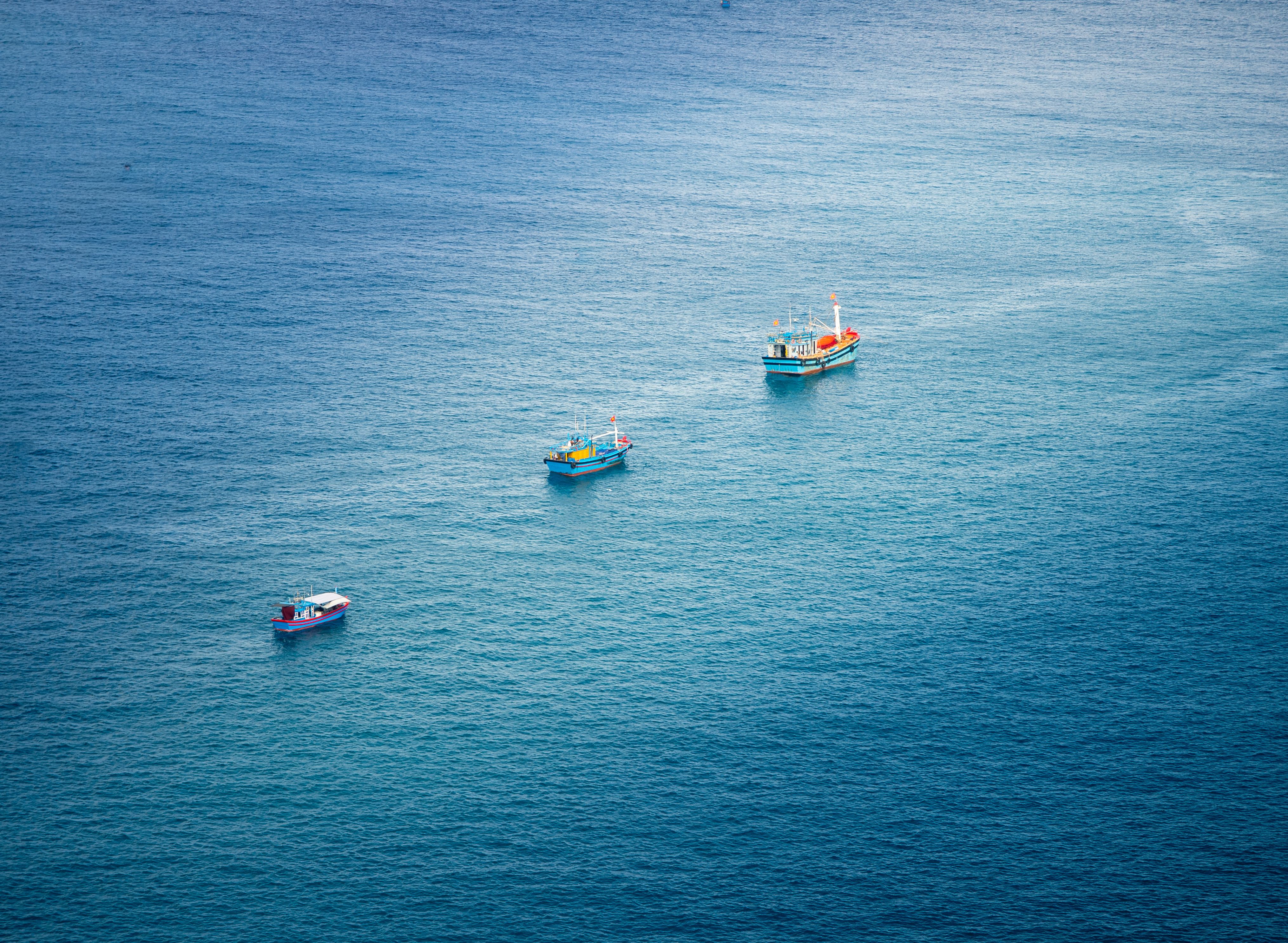 Aerial view of colorful fishing boats on the vibrant blue ocean in Hòa Xuân, Đắk Lắk, Vietnam.