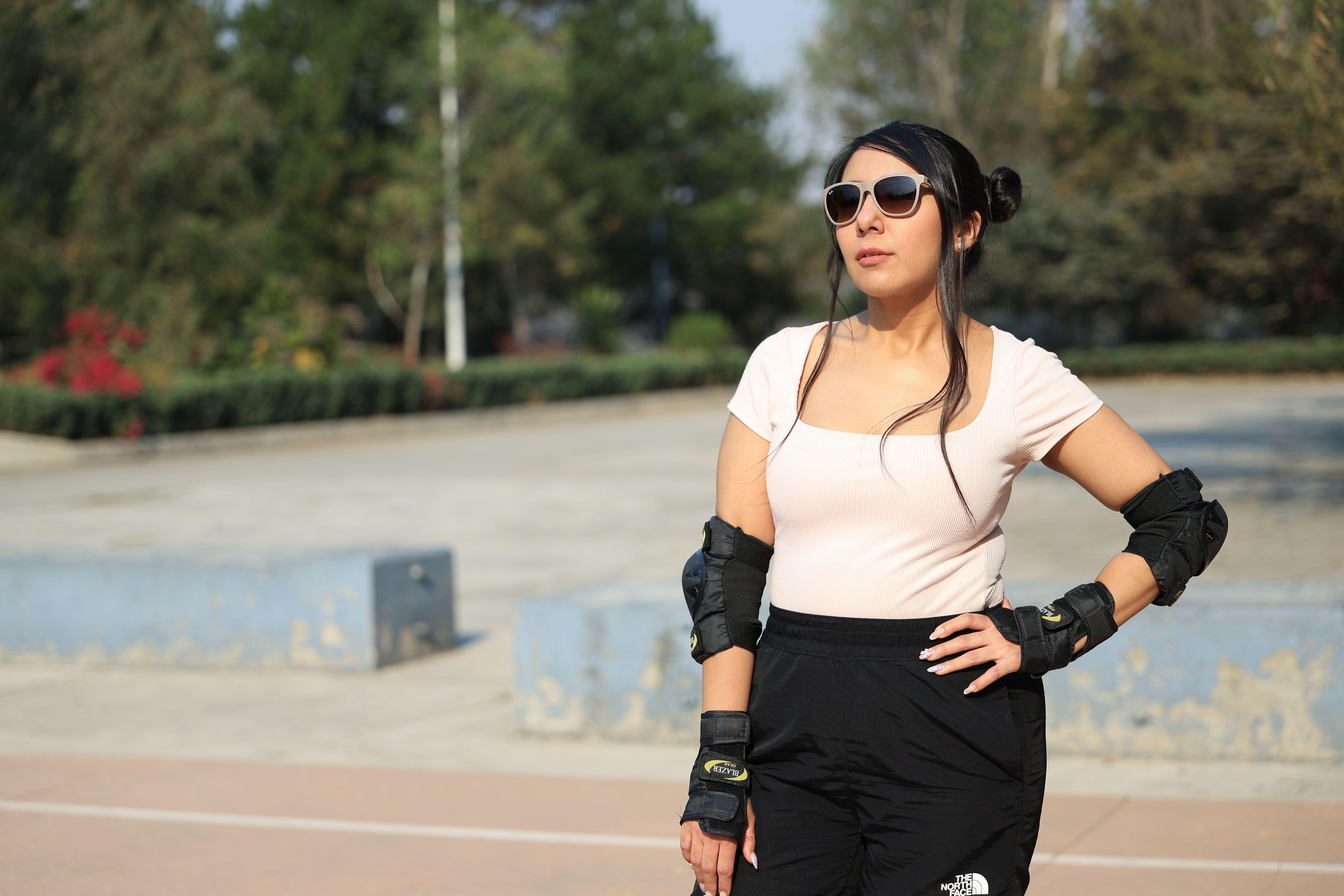 Woman wearing roller skating gear and sunglasses poses confidently in a sunny outdoor setting.