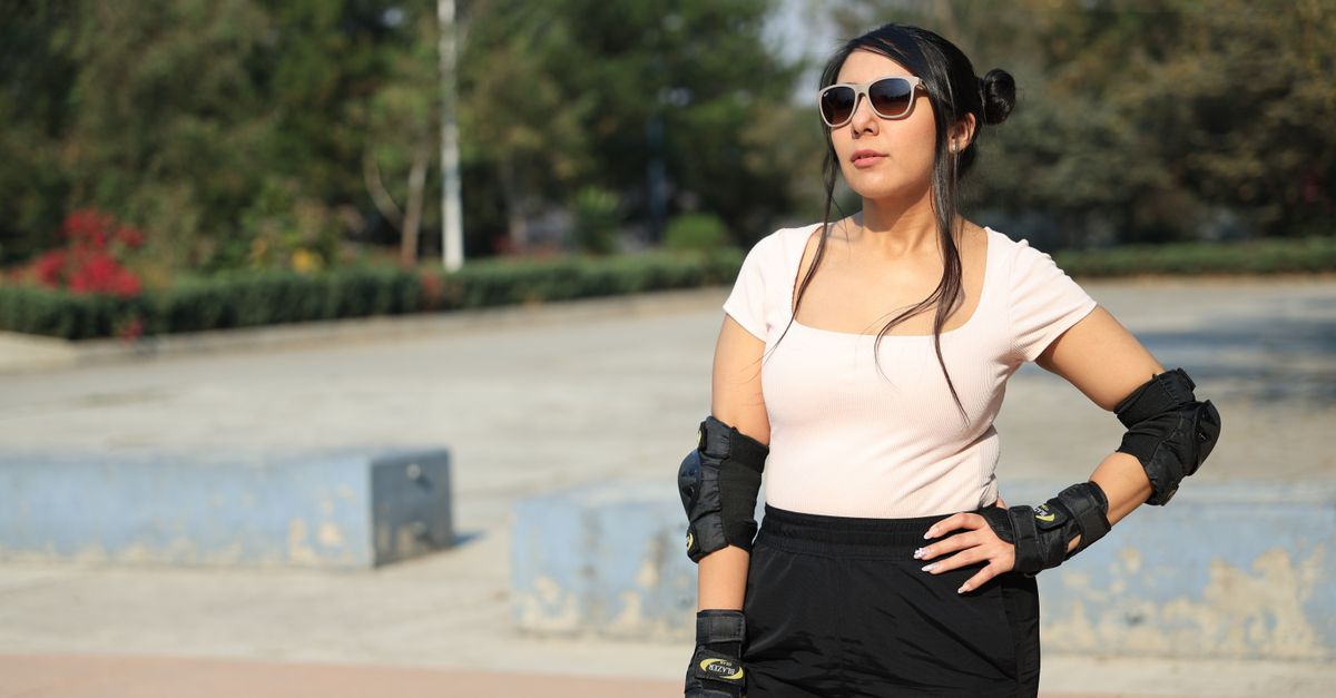 Woman wearing roller skating gear and sunglasses poses confidently in a sunny outdoor setting.