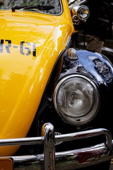 Close-up of a classic yellow and black VW Beetle's front headlight and bumper.