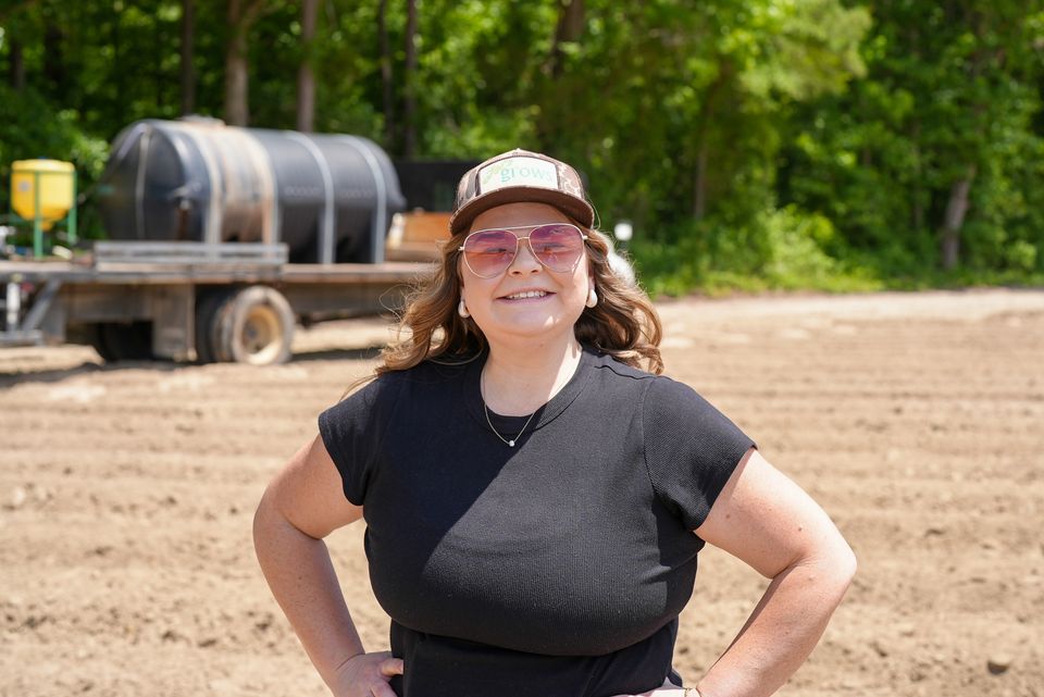 Woman farmer standing confidently in a field with agricultural machinery behind her