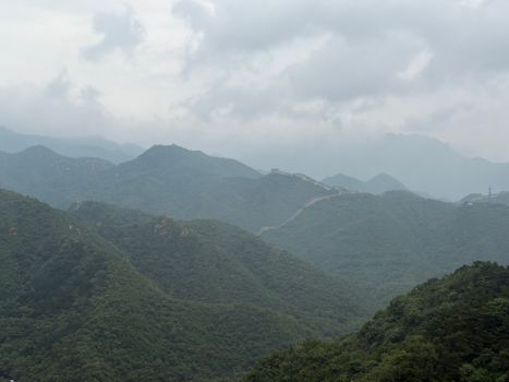 Misty landscape view of the Great Wall of China across lush green mountains.