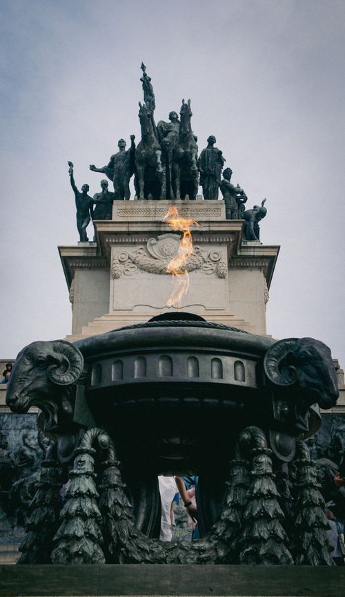 Free Statues atop a monument with an eternal flame burning brightly beneath, creating a dramatic effect. Stock Photo